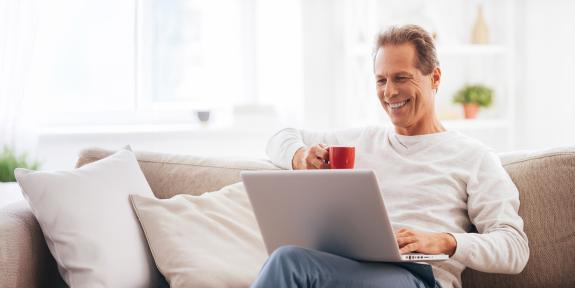 Mann mit Tasse und Laptop auf der Couch